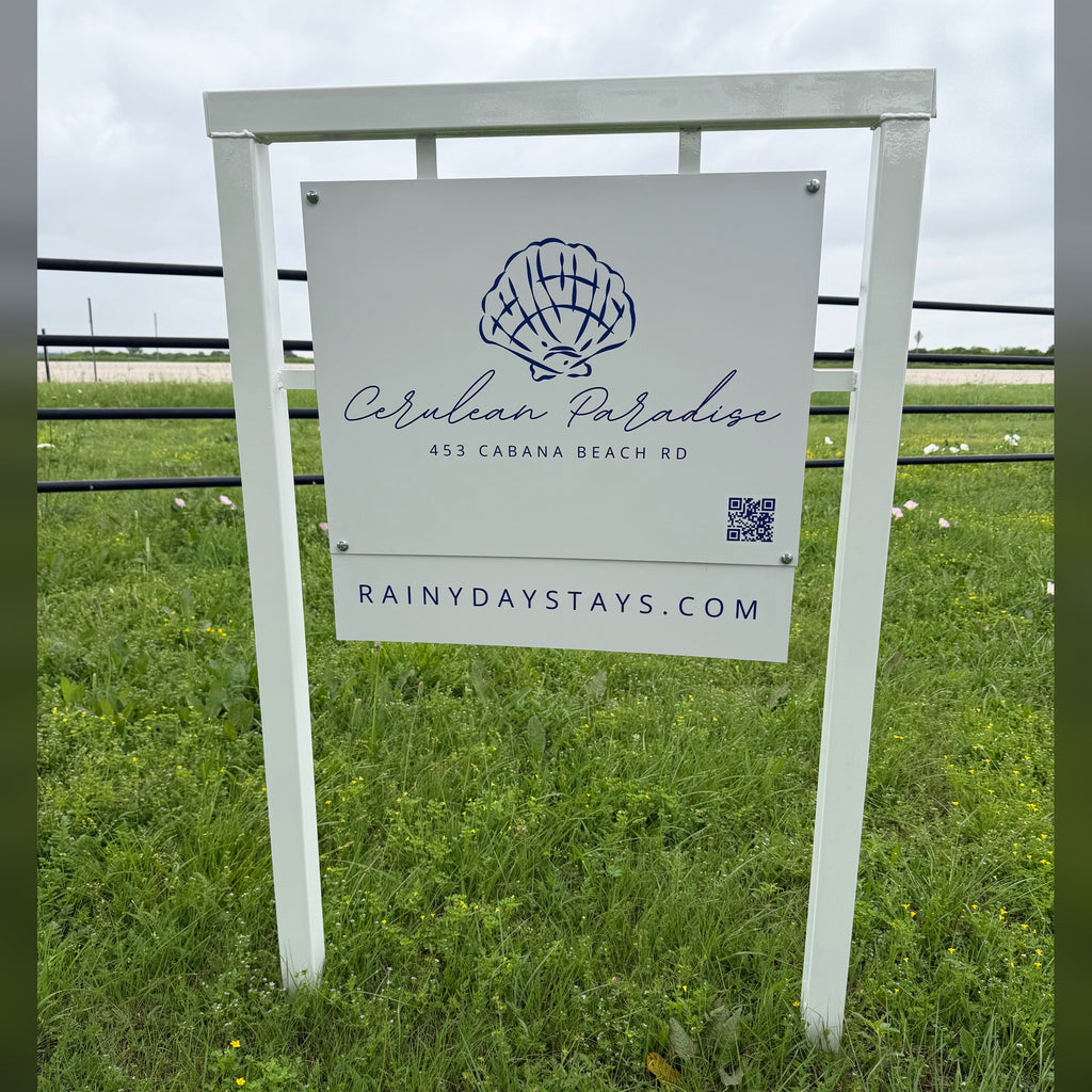 Cerulean Paradise beach rental road sign we built: white frame, shell logo panel with QR code and RainyDayStays.com website rider