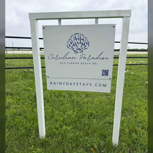 Cerulean Paradise beach rental road sign we built: white frame, shell logo panel with QR code and RainyDayStays.com website rider