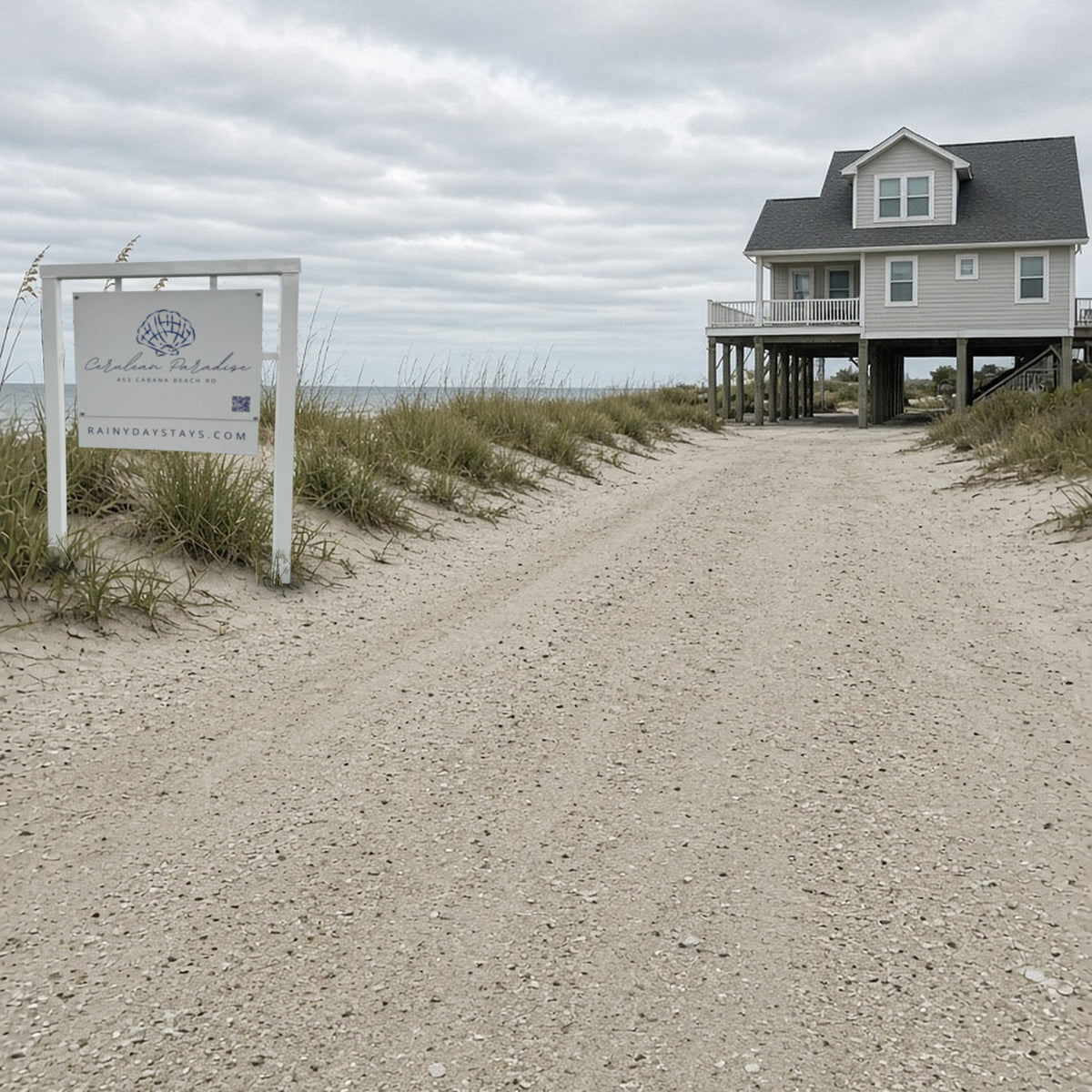 White beach house STR road sign with shell logo, QR code and website rider standing in the dune grass beside a sandy drive to a beach house (mockup of a real sign we built)