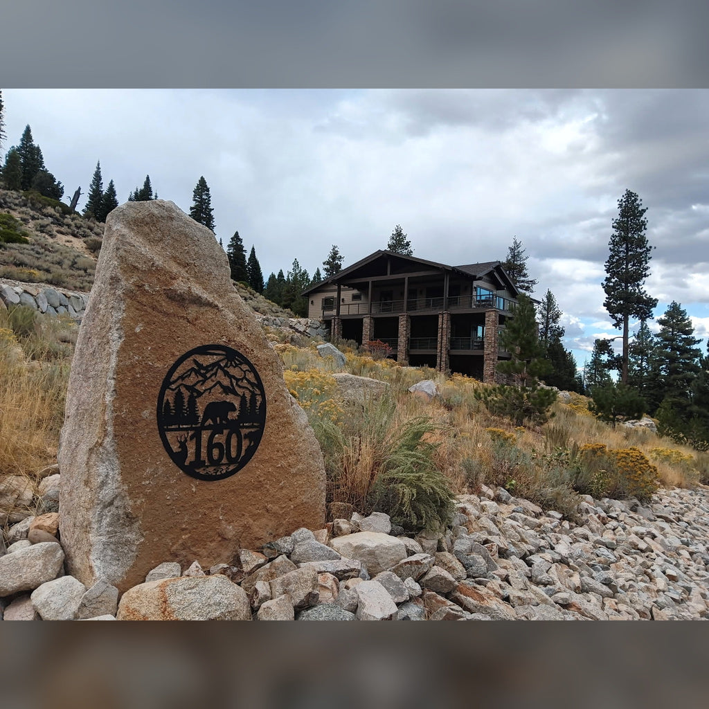 Round black bear and deer address sign with house number 160 installed on a granite boulder in front of a mountain home