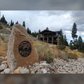 Round black bear and deer address sign with house number 160 installed on a granite boulder in front of a mountain home