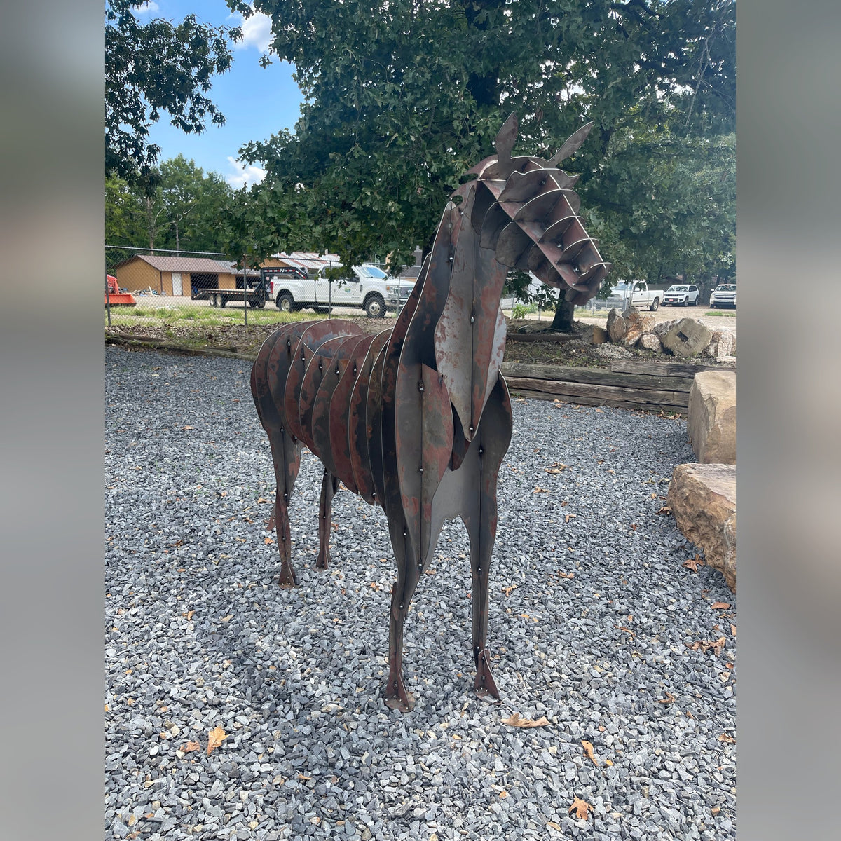 Rusted Corten steel horse sculpture standing on gravel