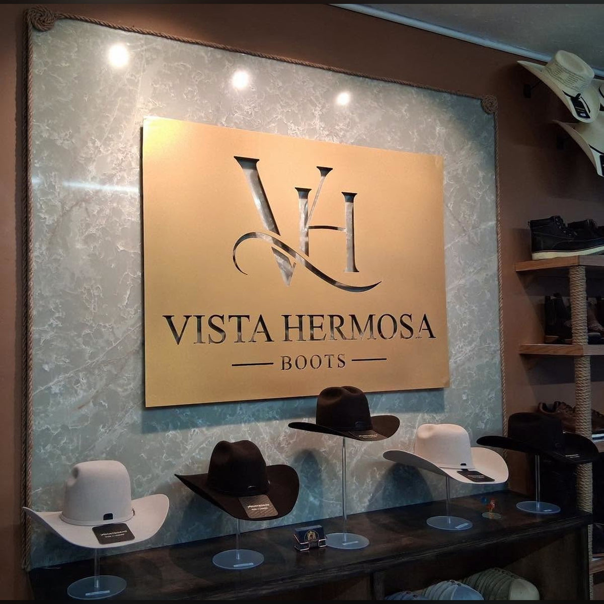 Gold powder-coated steel Vista Hermosa Boots logo sign panel on a boutique wall above a cowboy hat display